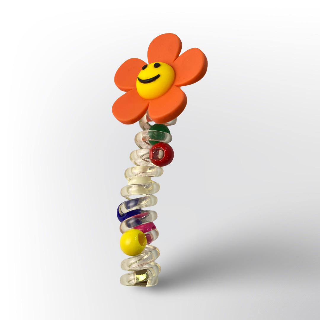 Resorte Moña con Flor 🌼 – Espiral transparente adornado con cuentas de colores y una divertida flor naranja con carita sonriente en la parte superior.